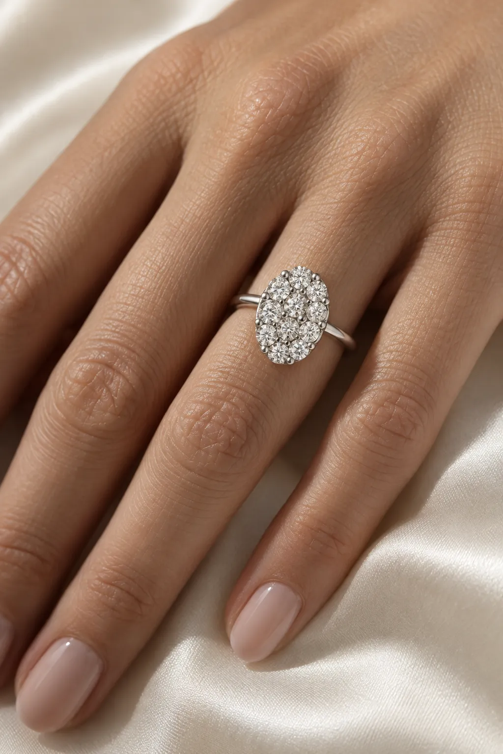 Oval cluster ring in white gold with closely set small brilliants on the ring finger, hand on light silk