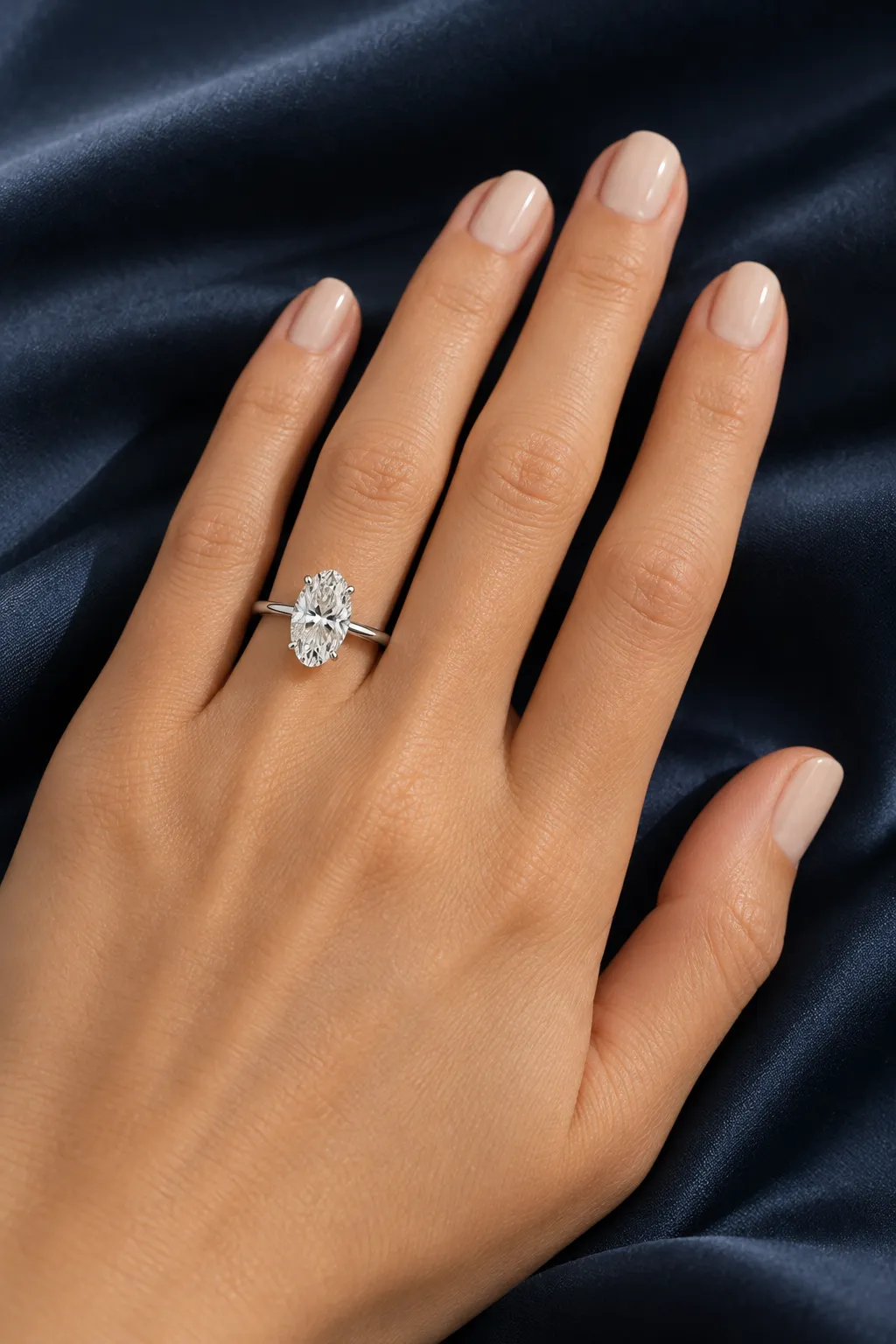 Hand auf Navy-Seide mit Moval-Verlobungsring in Platin am Ringfinger, der längliche Diamant streckt den Finger