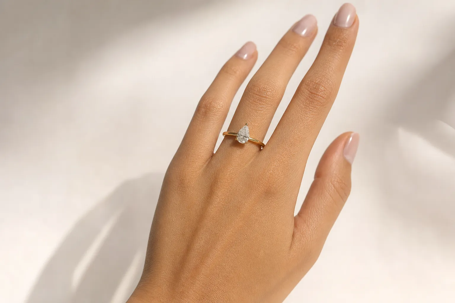 Ein Verlobungsring mit tropfenförmigem Pear-Cut-Diamant in Gelbgold an einer Hand, Spitze zeigt zur Fingerspitze