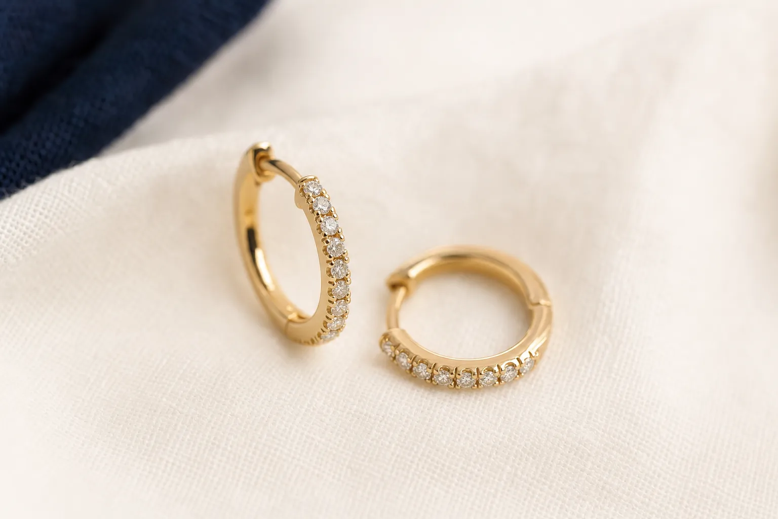 Ein Paar kleine Diamant-Creolen in Gelbgold auf warmem Leinen, Nahaufnahme