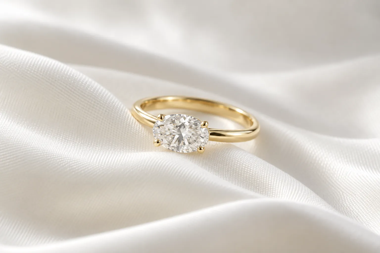 East-West-Verlobungsring in Gelbgold mit quer gefasstem ovalem Diamanten, die lange Seite des Steins folgt dem Band, auf heller Seide