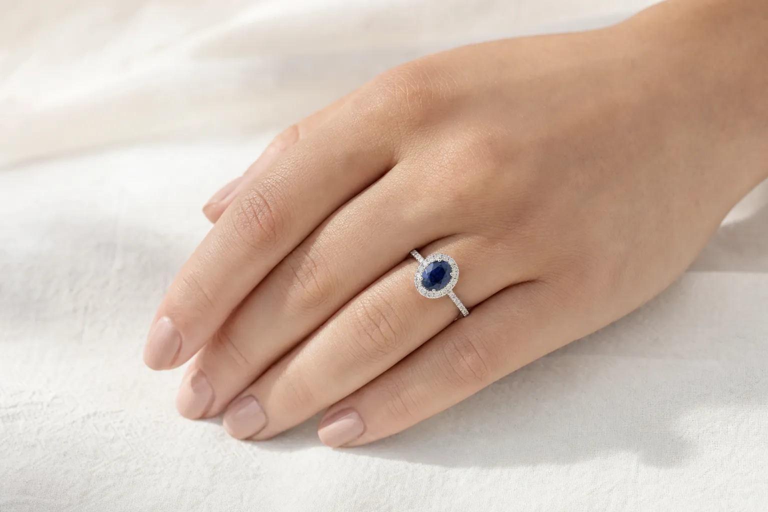 Oval geschliffener blauer Saphirring mit Diamanthalo in Weissgold, zum Vergleich mit farbigen Diamanten