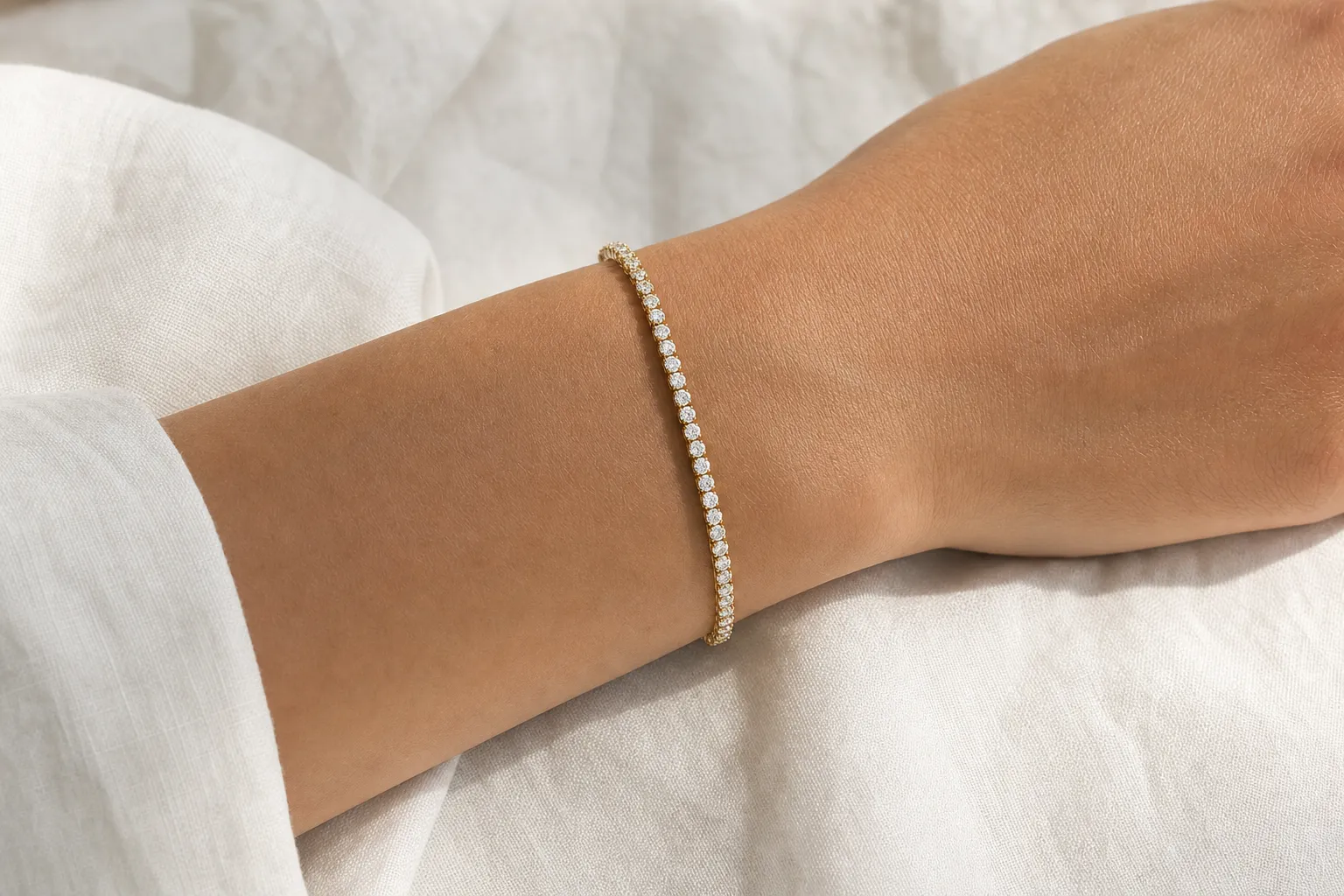 Diamant-Tennisarmband in Gelbgold an einem Damenhandgelenk auf weissem Leinen