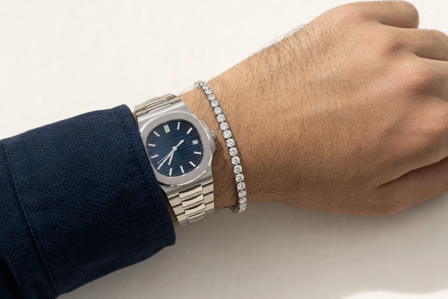 Tennisarmband mit etwas grösseren Steinen in Weissgold an einem Herrenhandgelenk neben einer Stahluhr