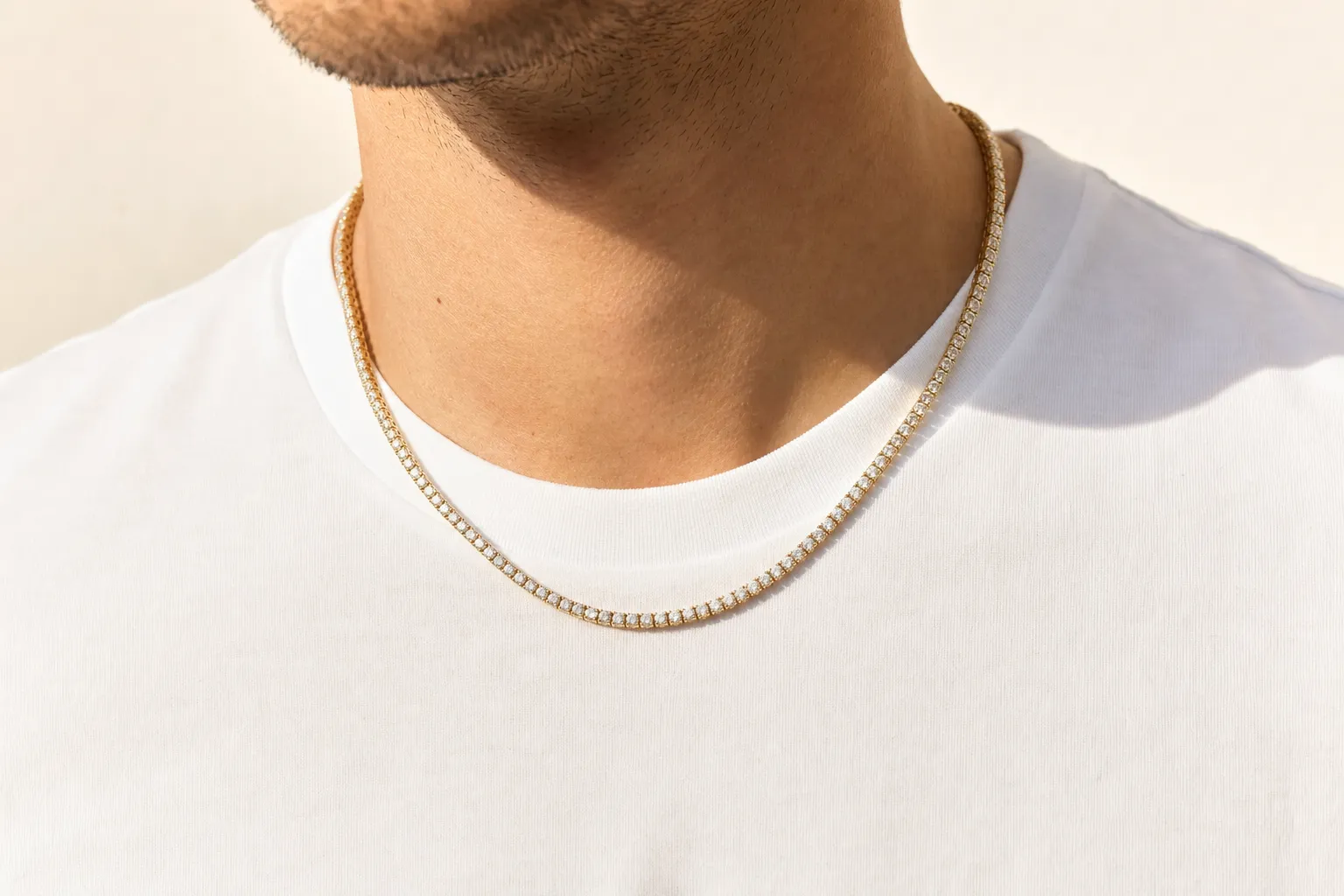 Une chaîne tennis portée sur le cou d'un homme au-dessus d'un t-shirt blanc uni