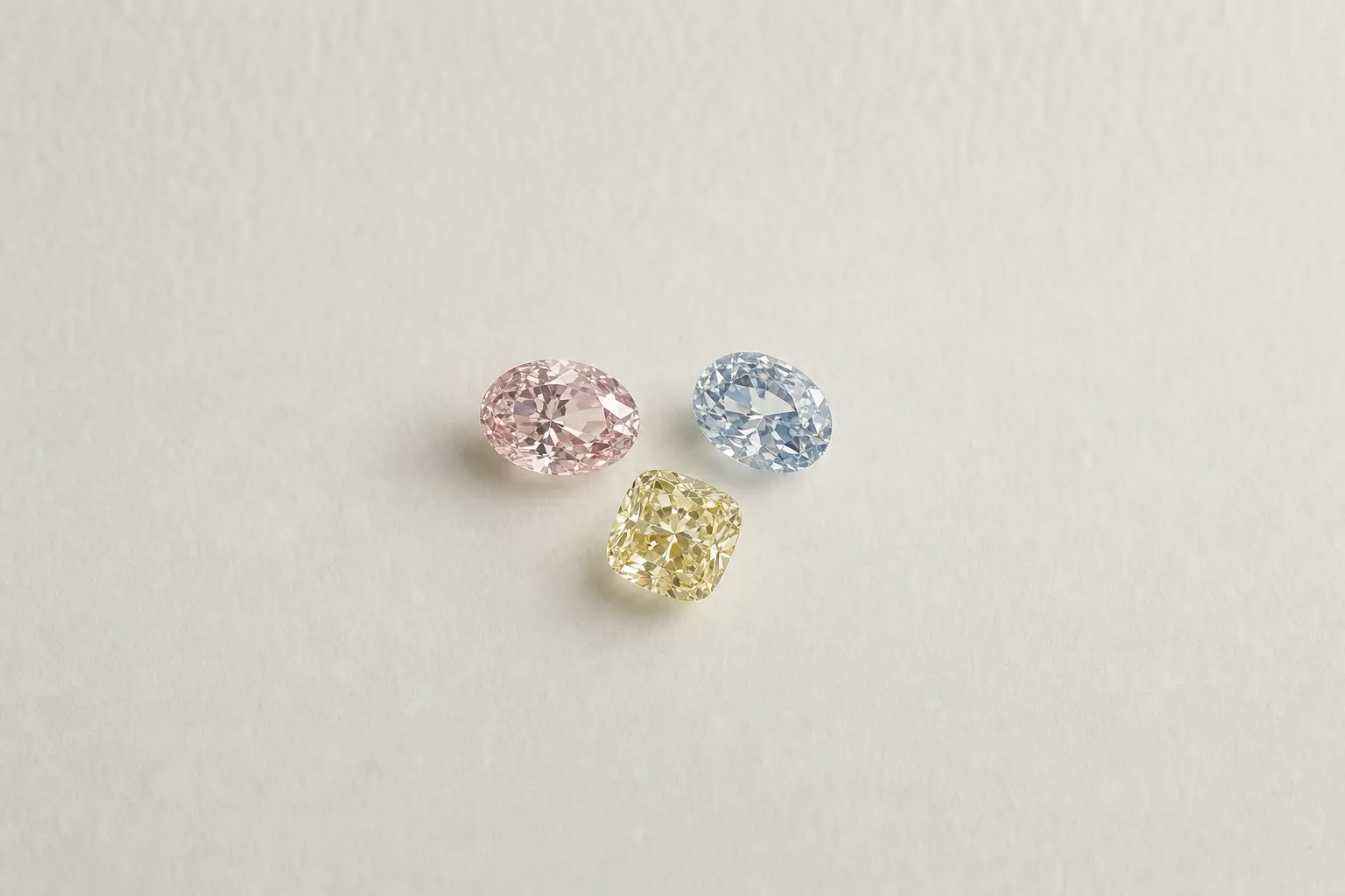 Drei lose Diamanten in Pink, Blau und Gelb nebeneinander auf hellem Papier