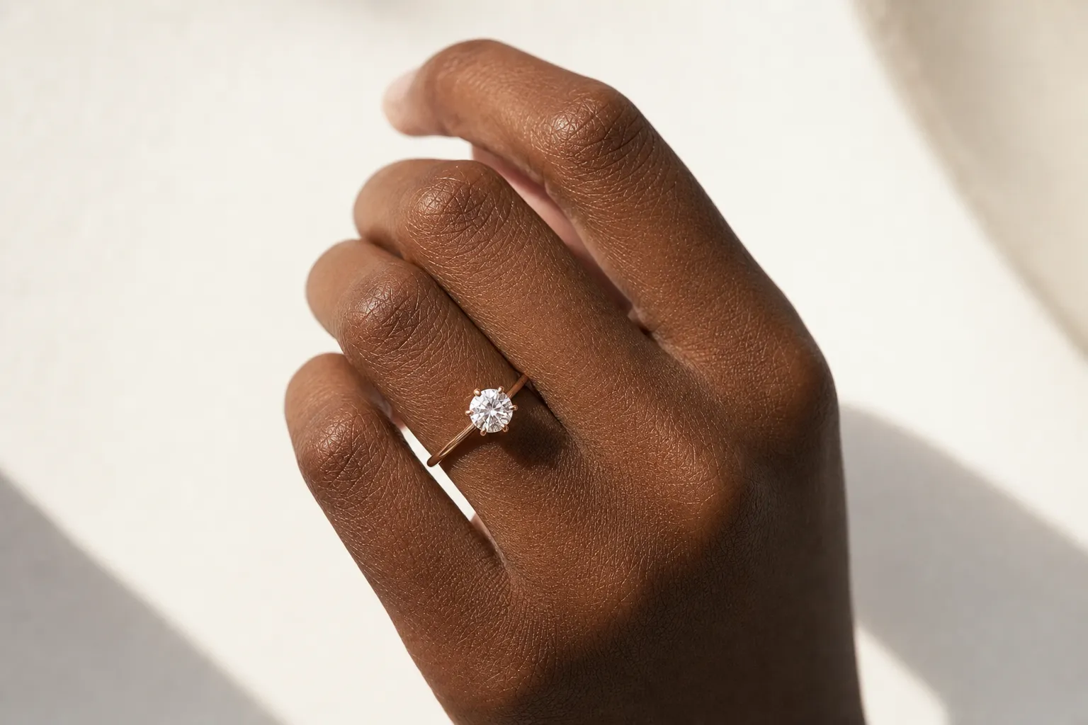 Verlobungsring in Roségold an einer Hand mit dunklem Hautton, Nahaufnahme bei Tageslicht