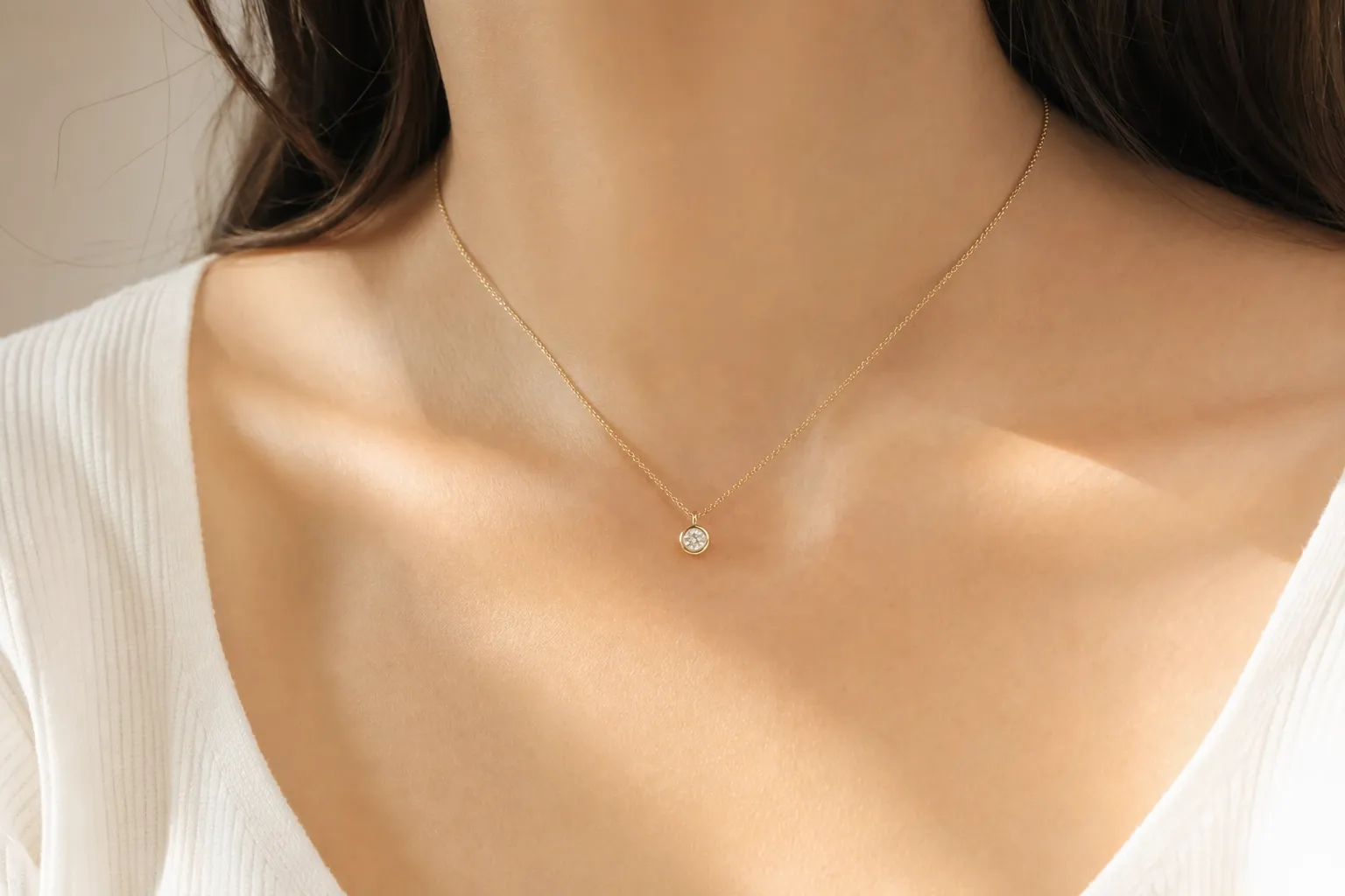 Une fine chaîne en or jaune avec un pendentif diamant rond en serti clos au niveau de la clavicule