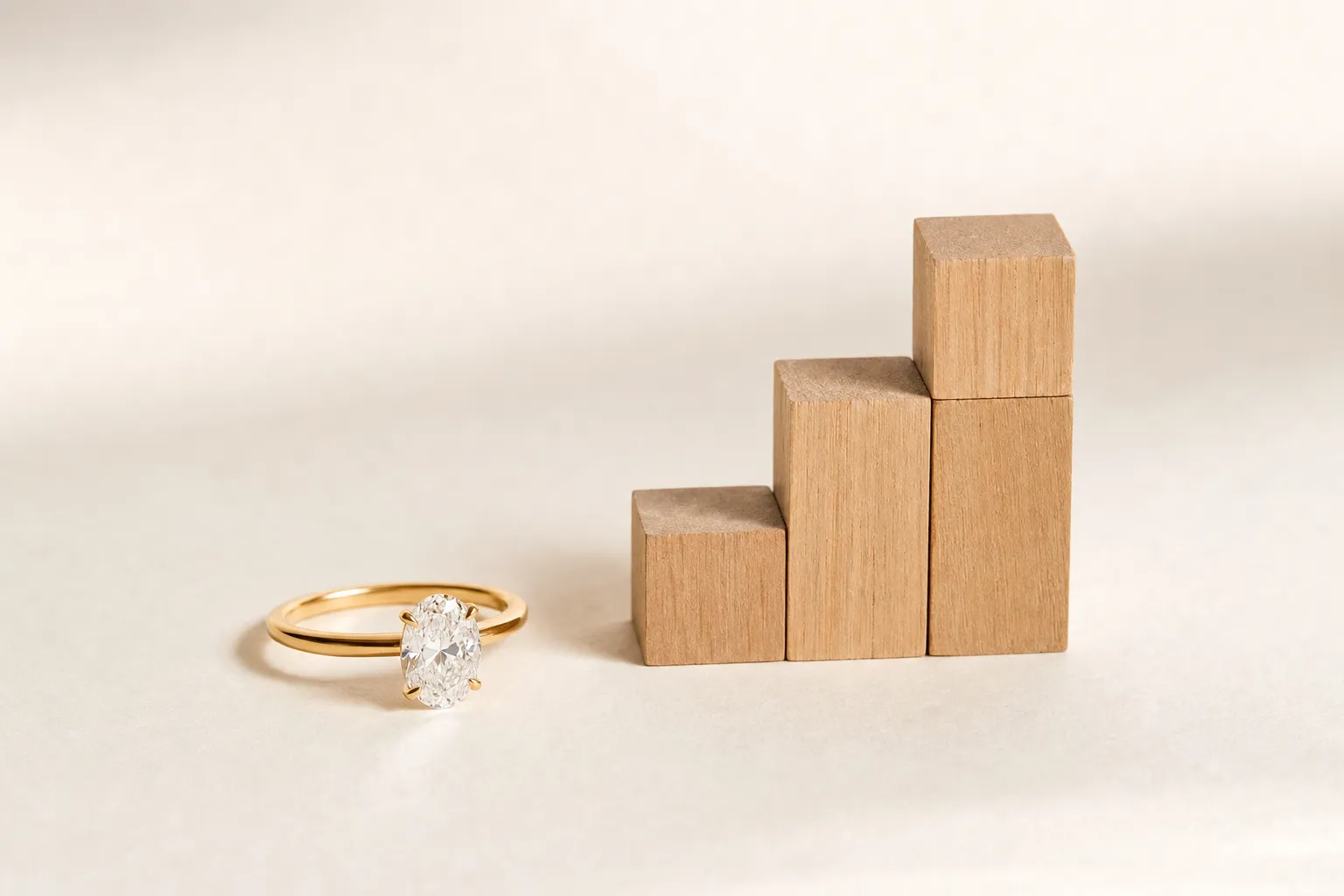 A diamond ring next to three small wooden blocks of increasing height on a bright surface