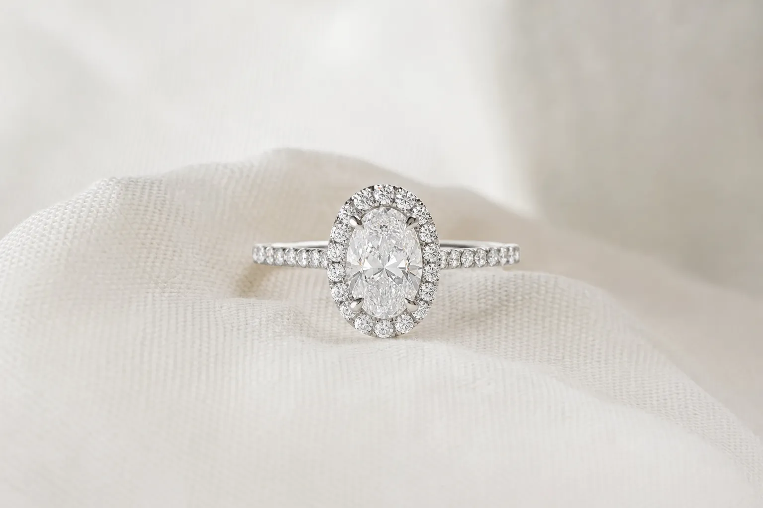 Halo-Verlobungsring mit ovalem Mittelstein, umgeben von kleinen Diamanten, in Weissgold auf weissem Leinen